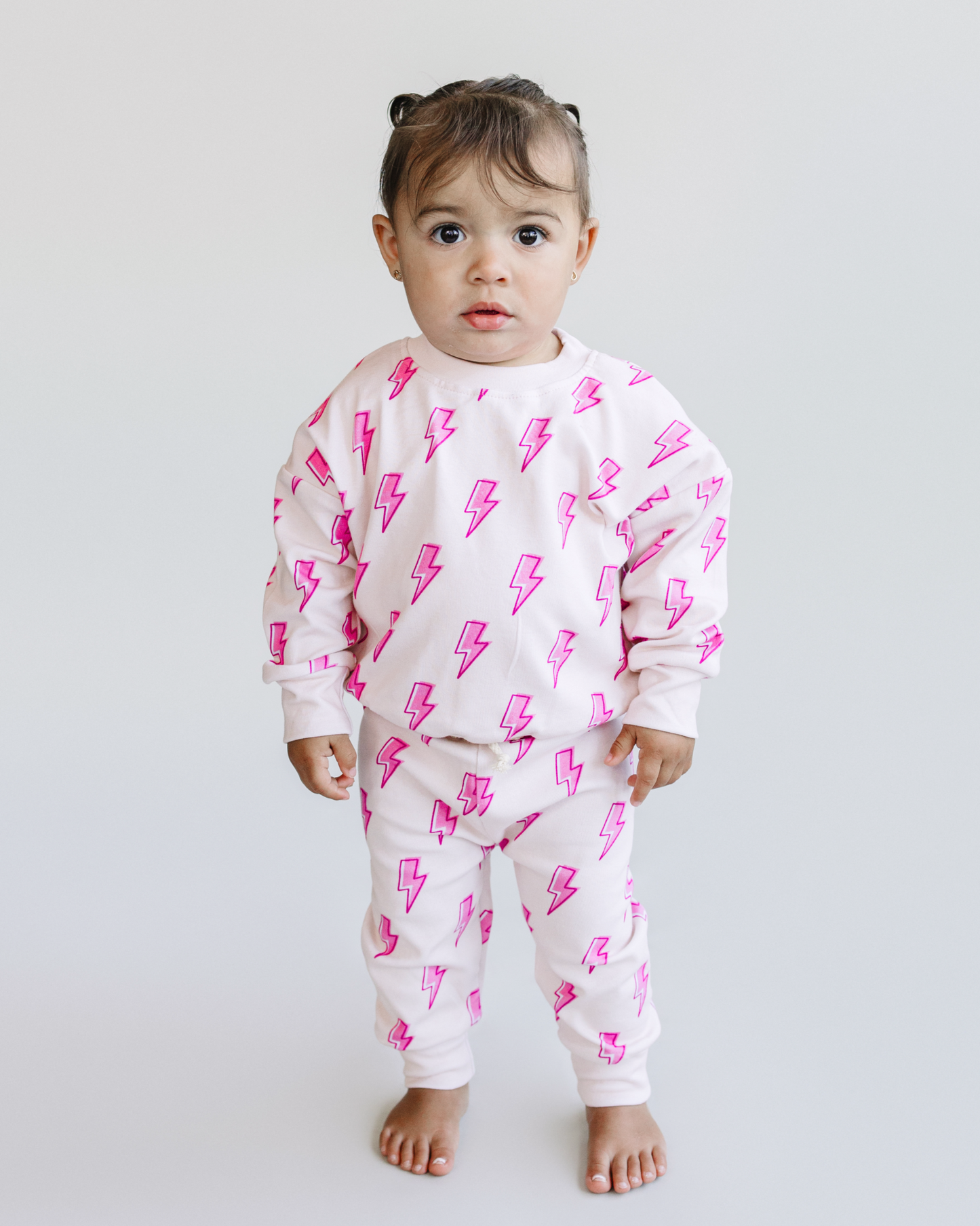 Child wearing a white outfit with pink lightning bolt patterns on a plain background