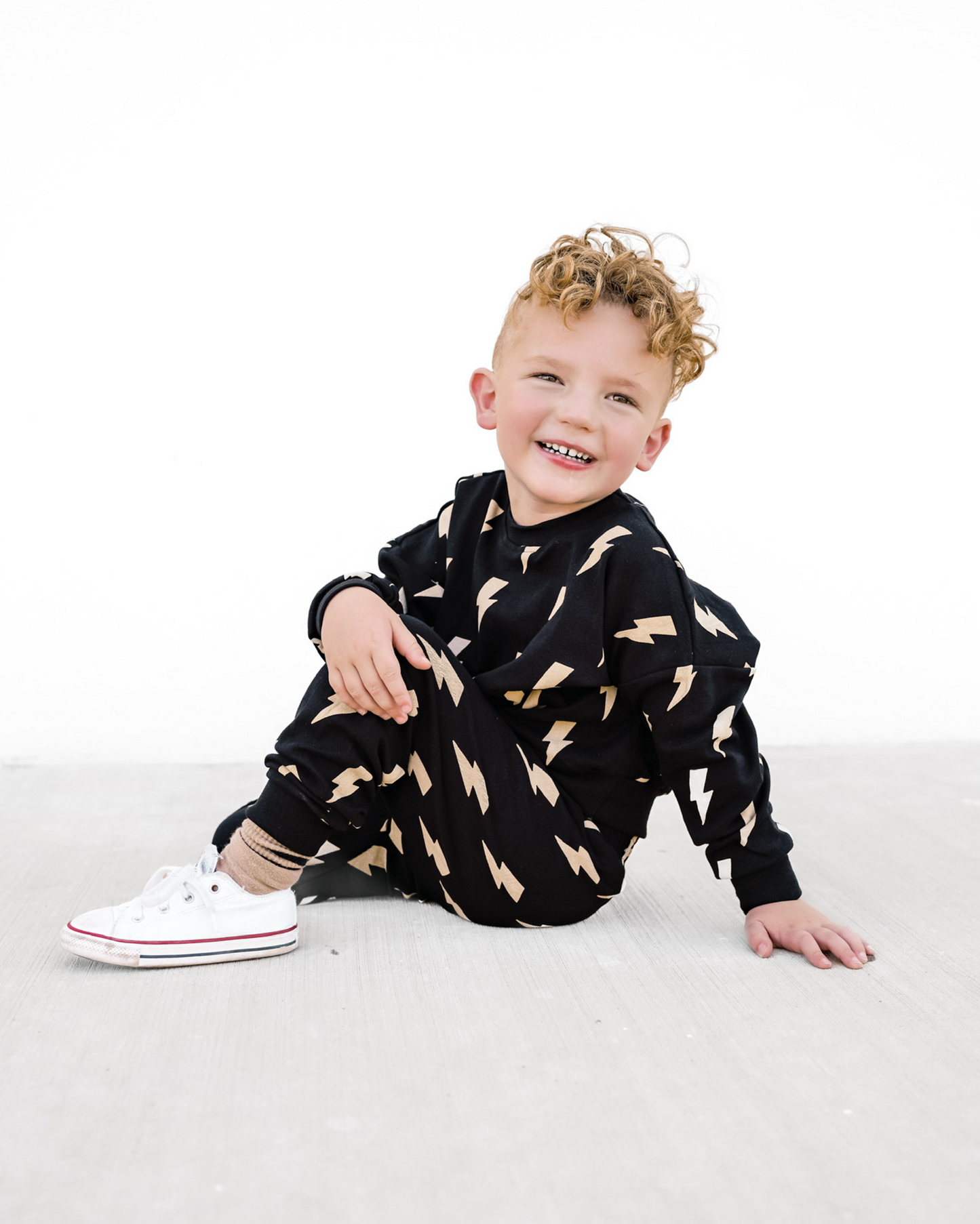 Child wearing a black outfit with gold patterns sitting on a white surface