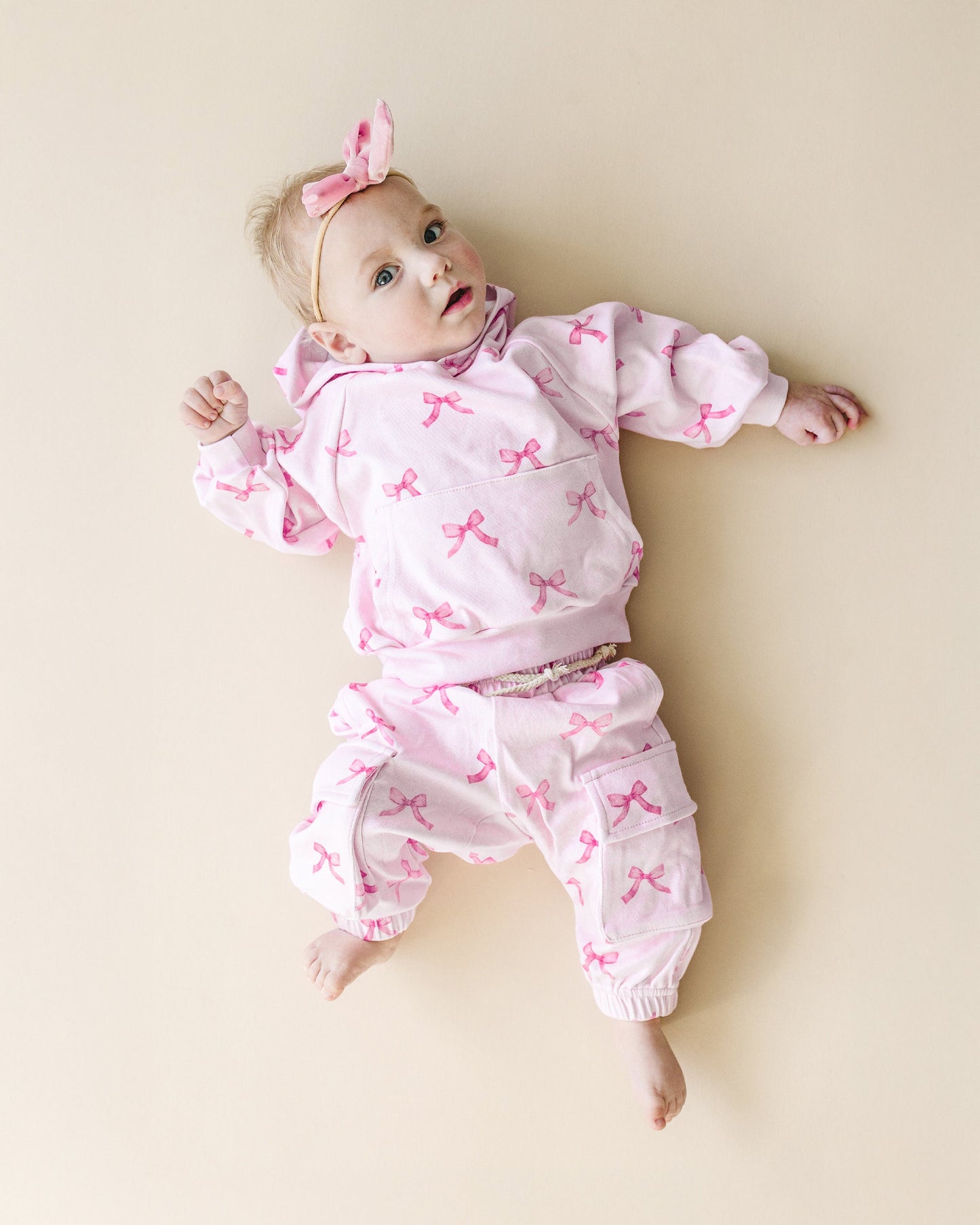 Baby wearing a pink outfit with bow patterns on a beige background