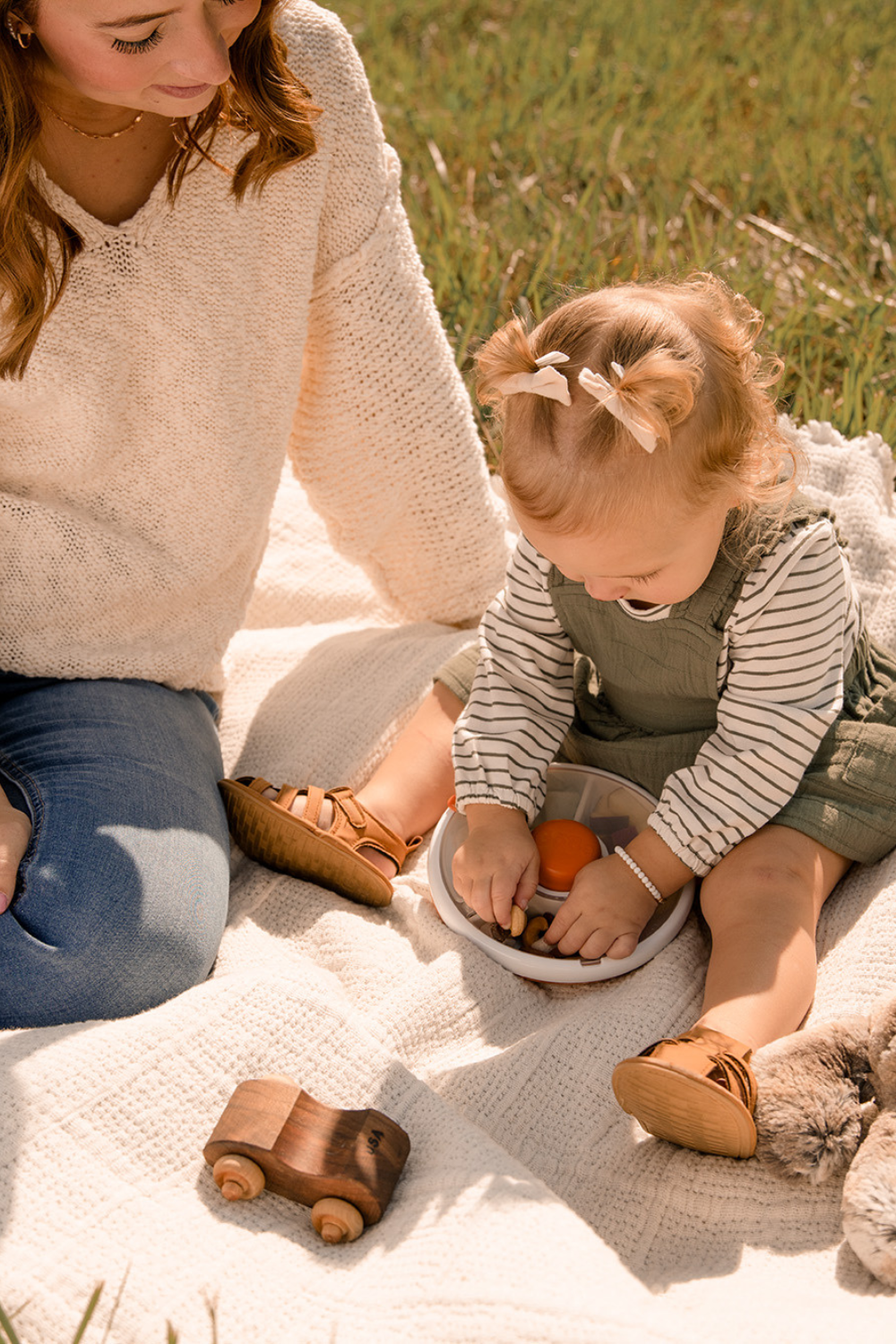 Woman and child sitting on a blanket outdoors, with the child holding a snack spinner.