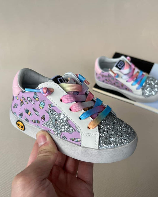 Child's shoe with colorful design held by a hand, with another shoe in the background on a surface.