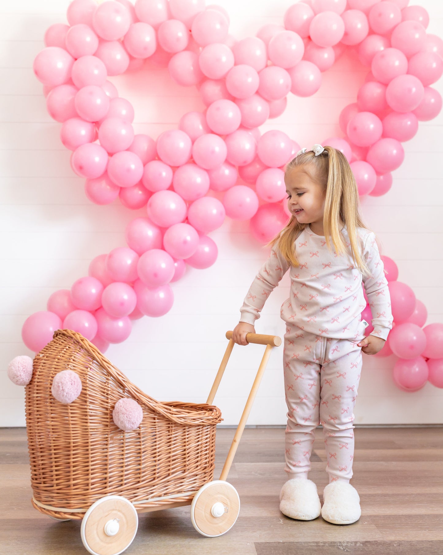 Child with a doll pram in front of pink balloon decorations shaped like hearts.