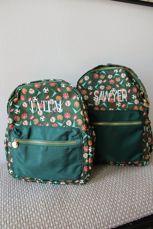 Two green backpacks with sports-themed patterns and embroidered names on a gray surface.