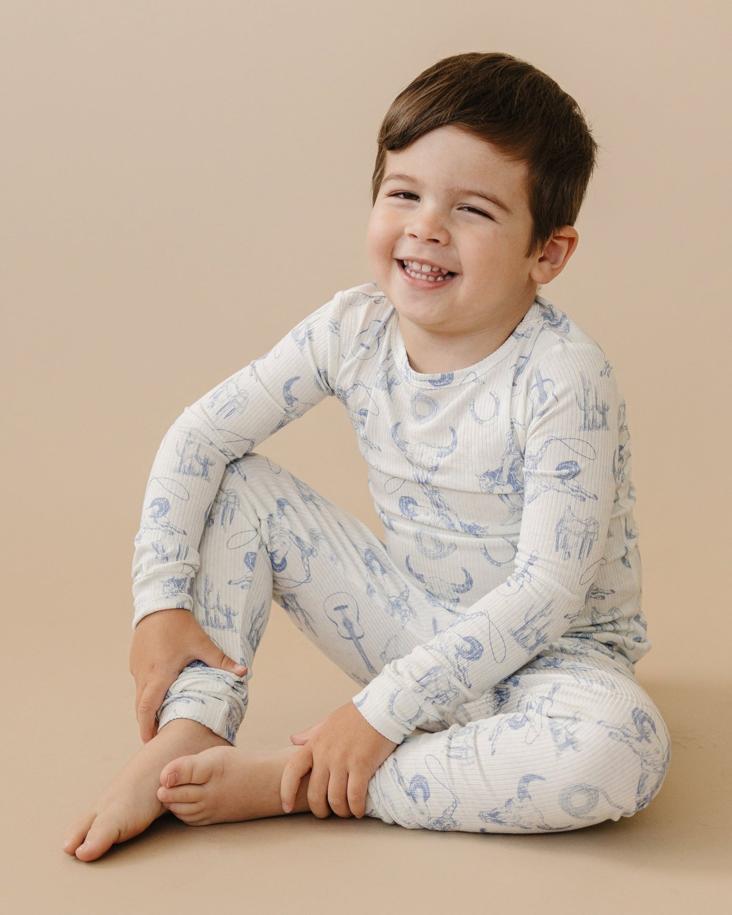Child wearing a white long-sleeve shirt and pants with blue patterns on a beige background