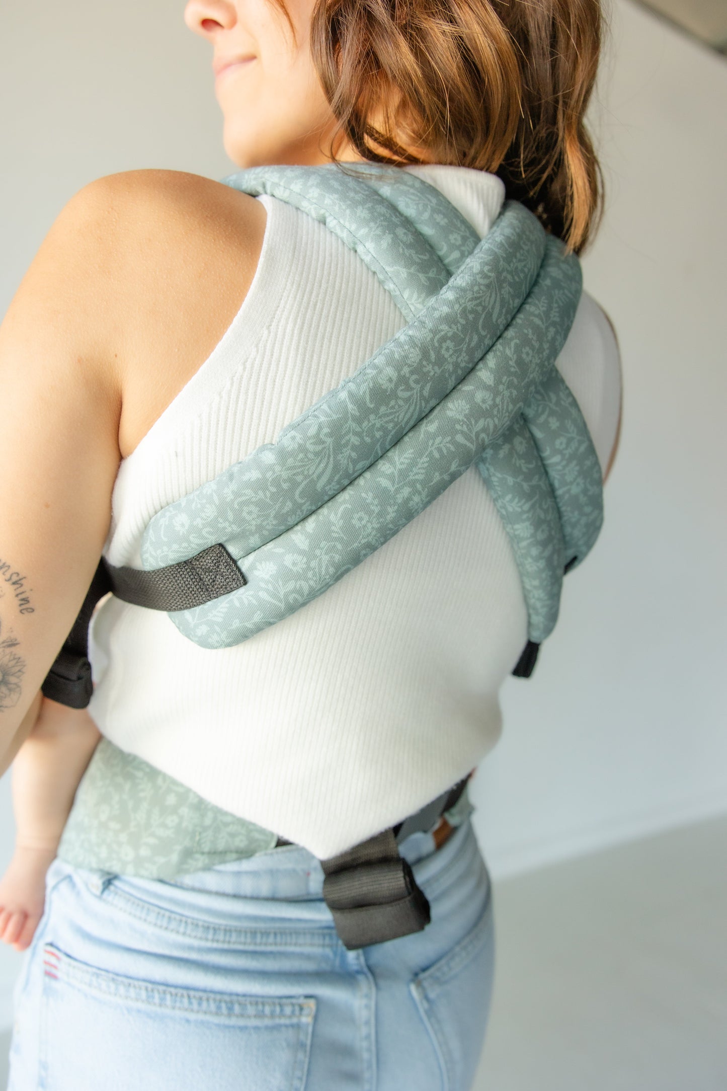 Person wearing a light green baby carrier on a plain background