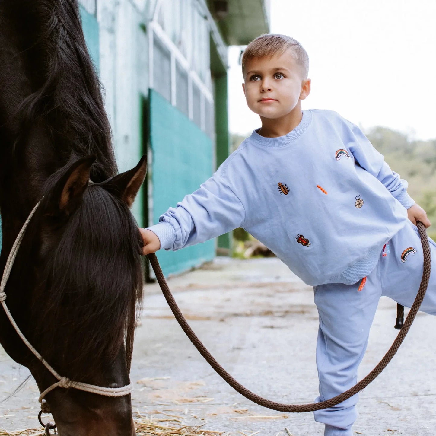 Child in a light blue outfit standing next to a horse, holding its reins.