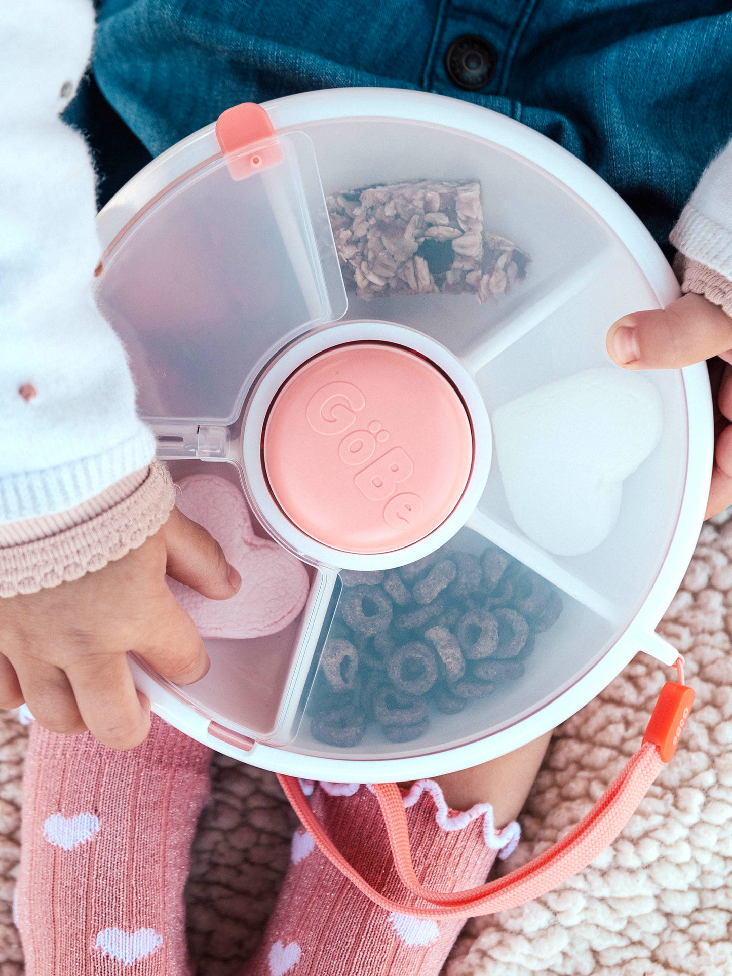 Children's hands holding a round, divided container with pink and white design.