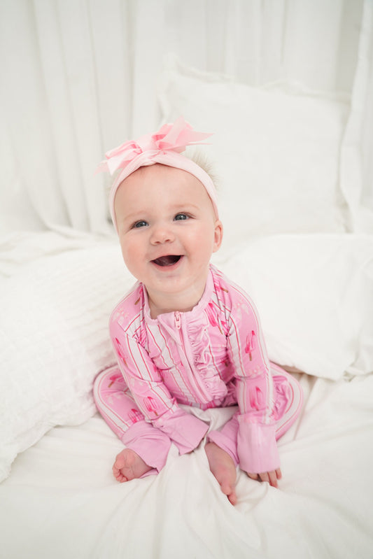 Baby wearing a pink outfit and headband sitting on a white blanket