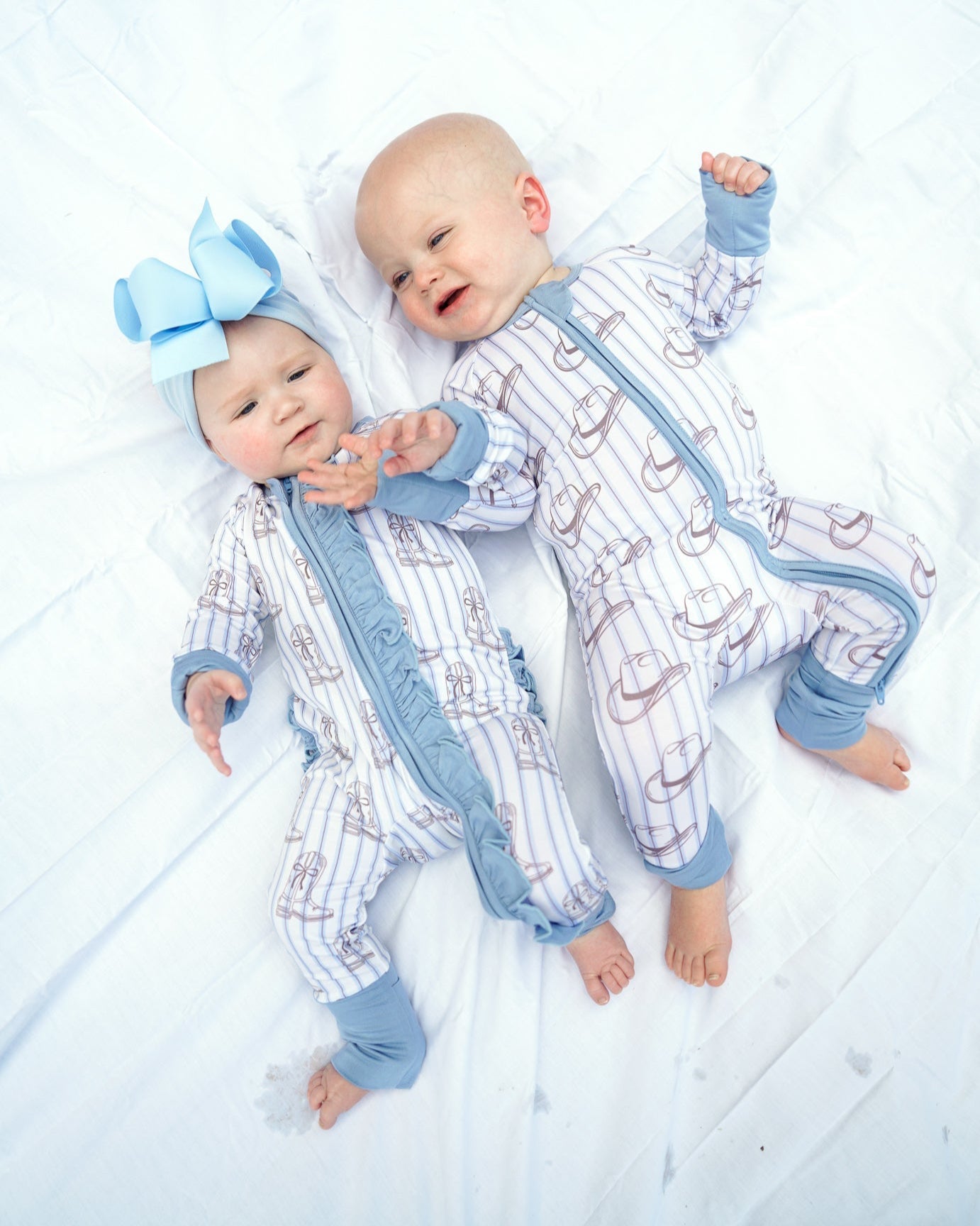 Two babies in matching outfits with a large bow on a white floor.