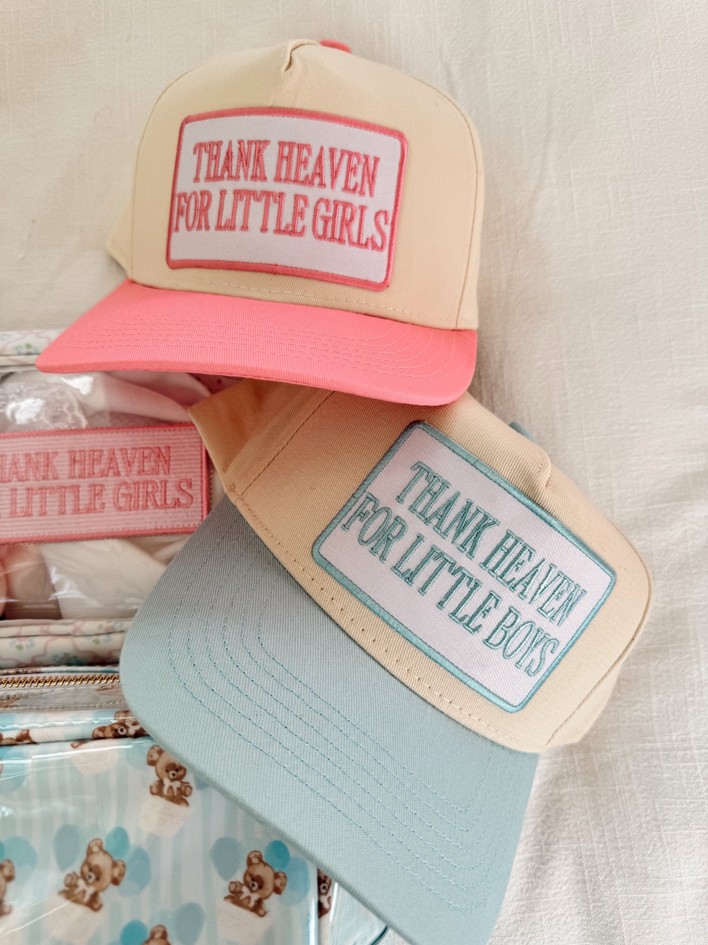 Two hats with text 'Thank Heaven for Little Girls' and 'Thank Heaven for Little Boys' on a neutral background.