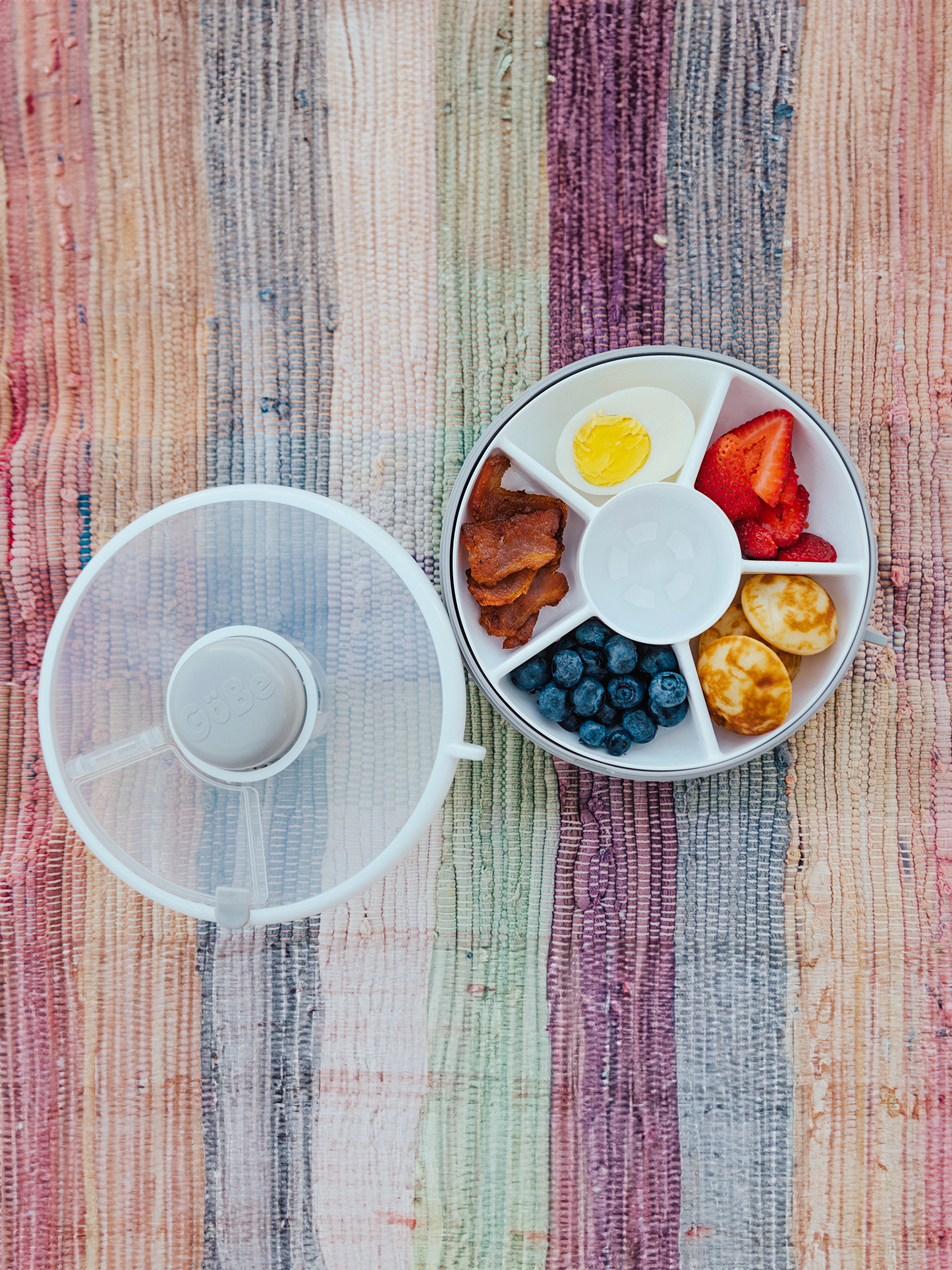 Round white plate with compartments containing food on a multicolored striped fabric background