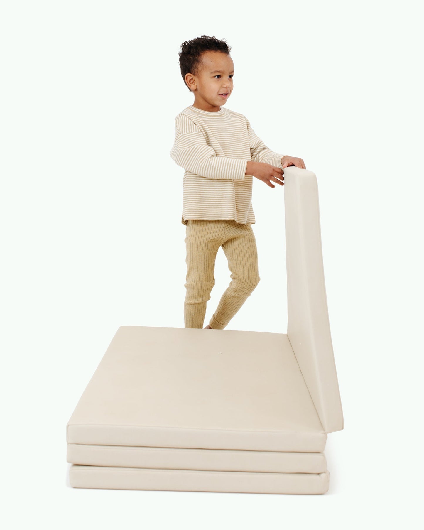 Child playing with a beige mattress on a white background