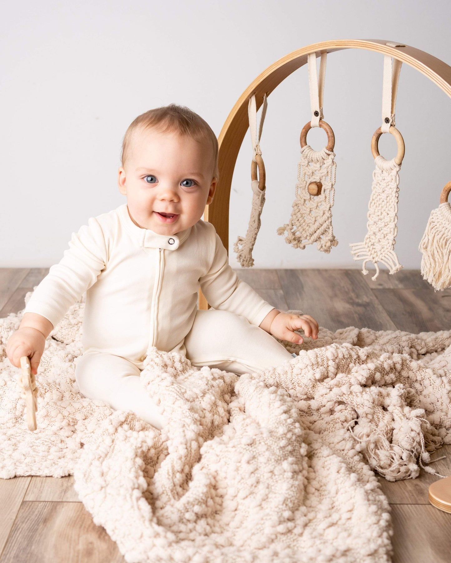 Baby sitting on a wooden floor with a baby gym and toys in the background