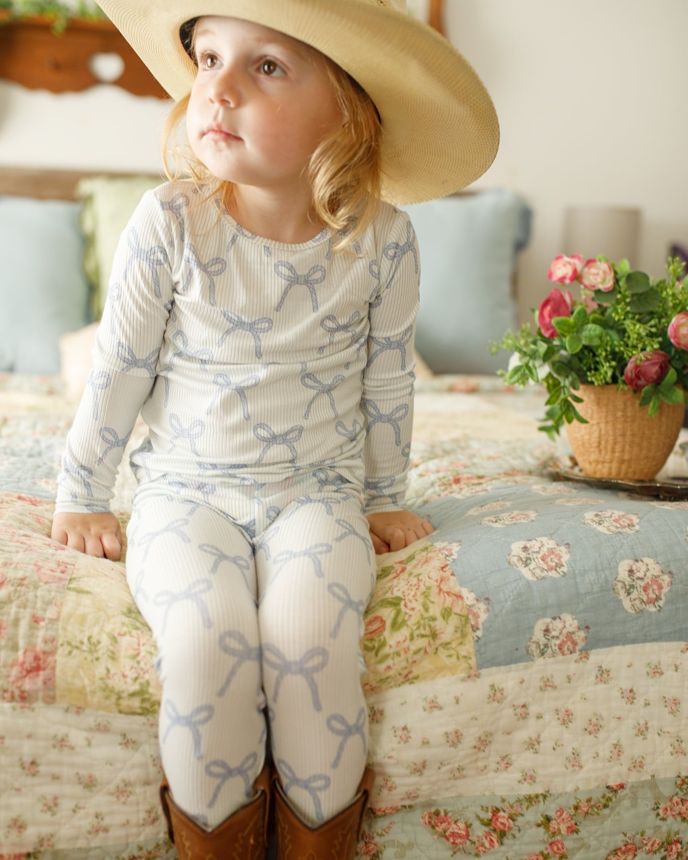 Child wearing a straw hat and patterned outfit sitting on a floral bedspread.