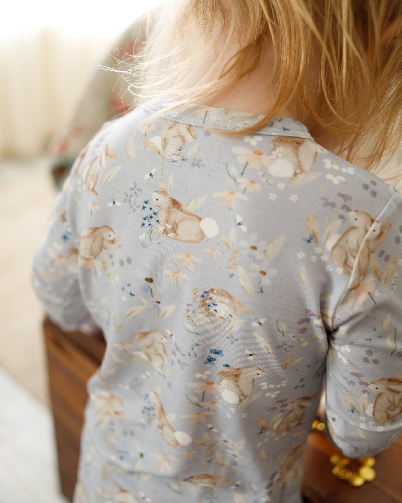Child wearing a light blue long-sleeve shirt with bunny prints in a home setting