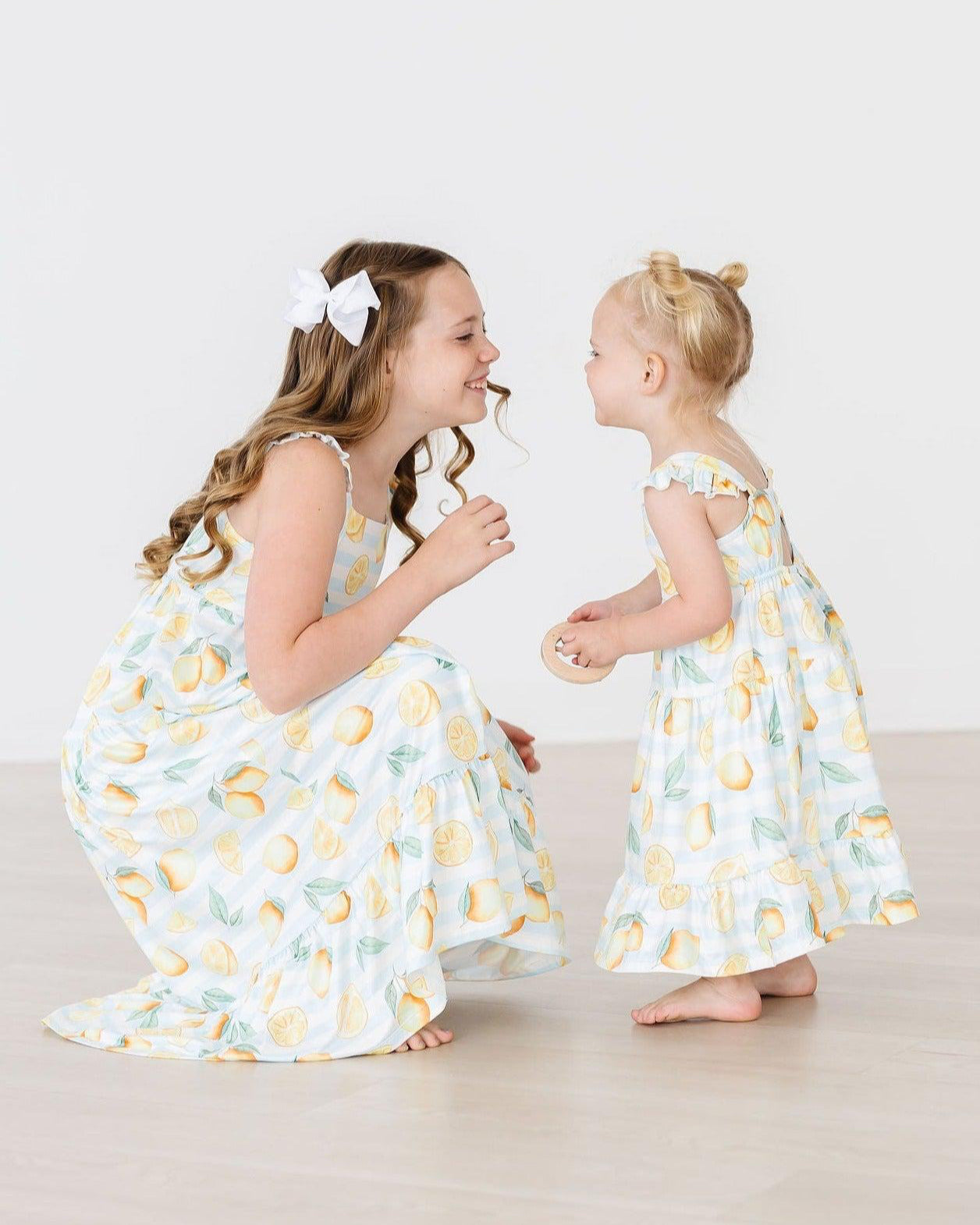 Two young girls in matching dresses with lemon pattern on a white background