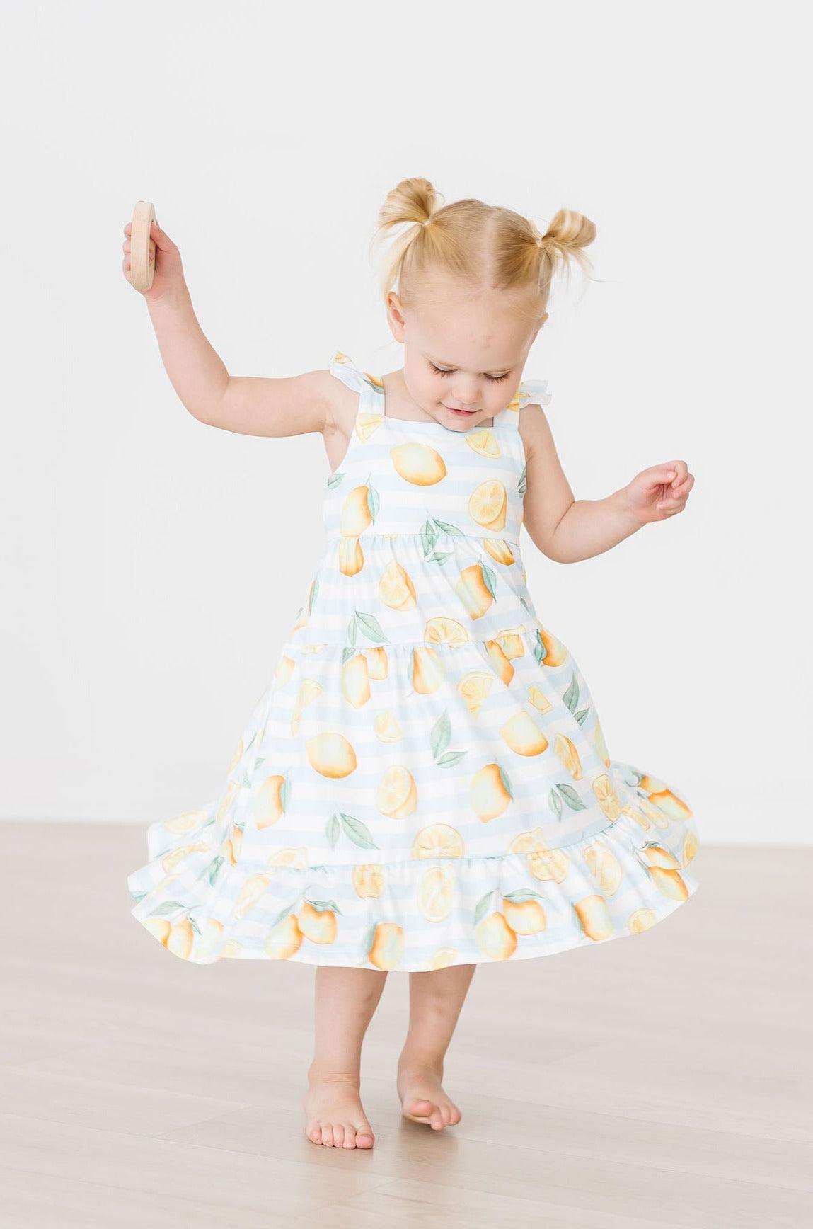 Young girl wearing a dress with lemon pattern on a plain background