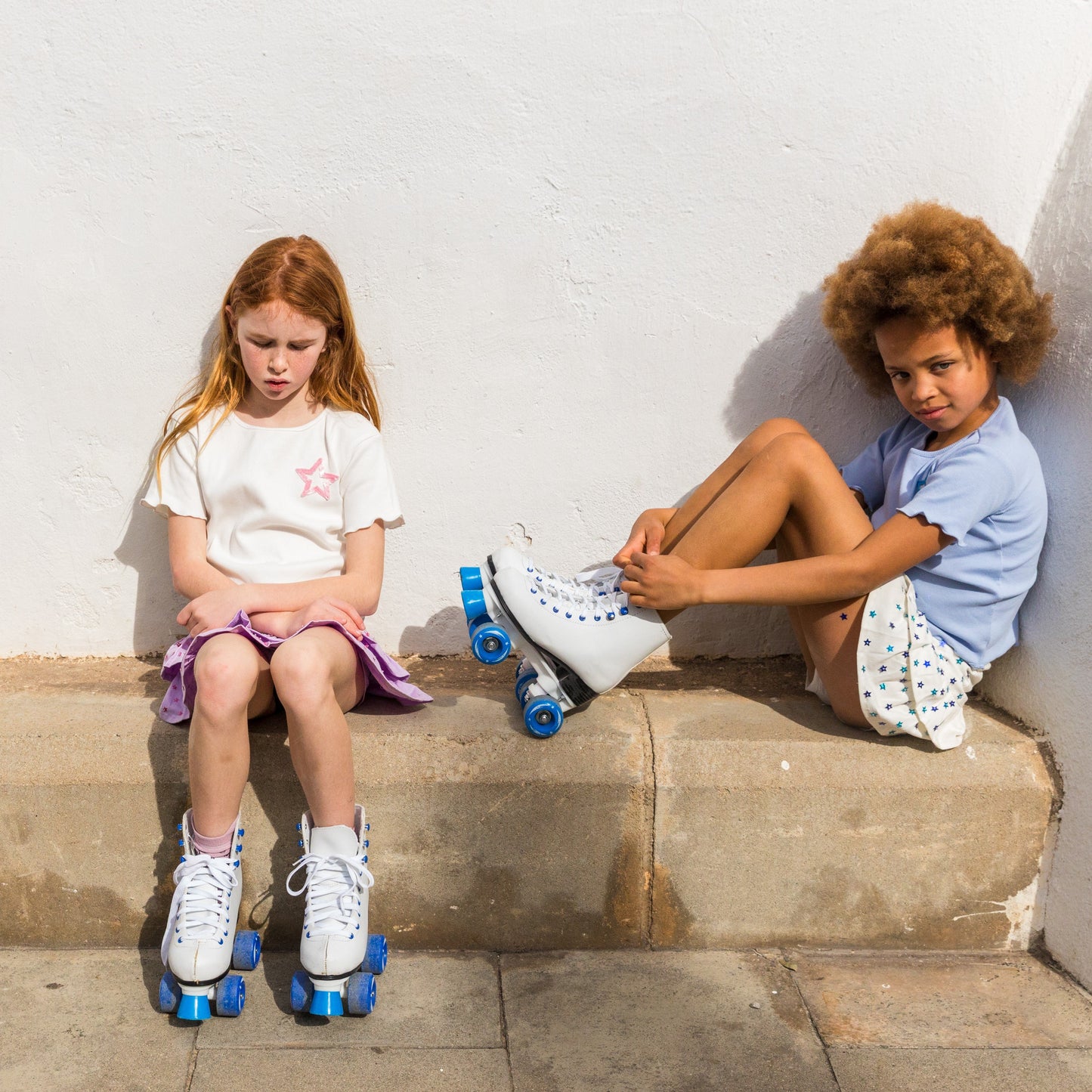 Two children sitting on a stone ledge with roller skates on.