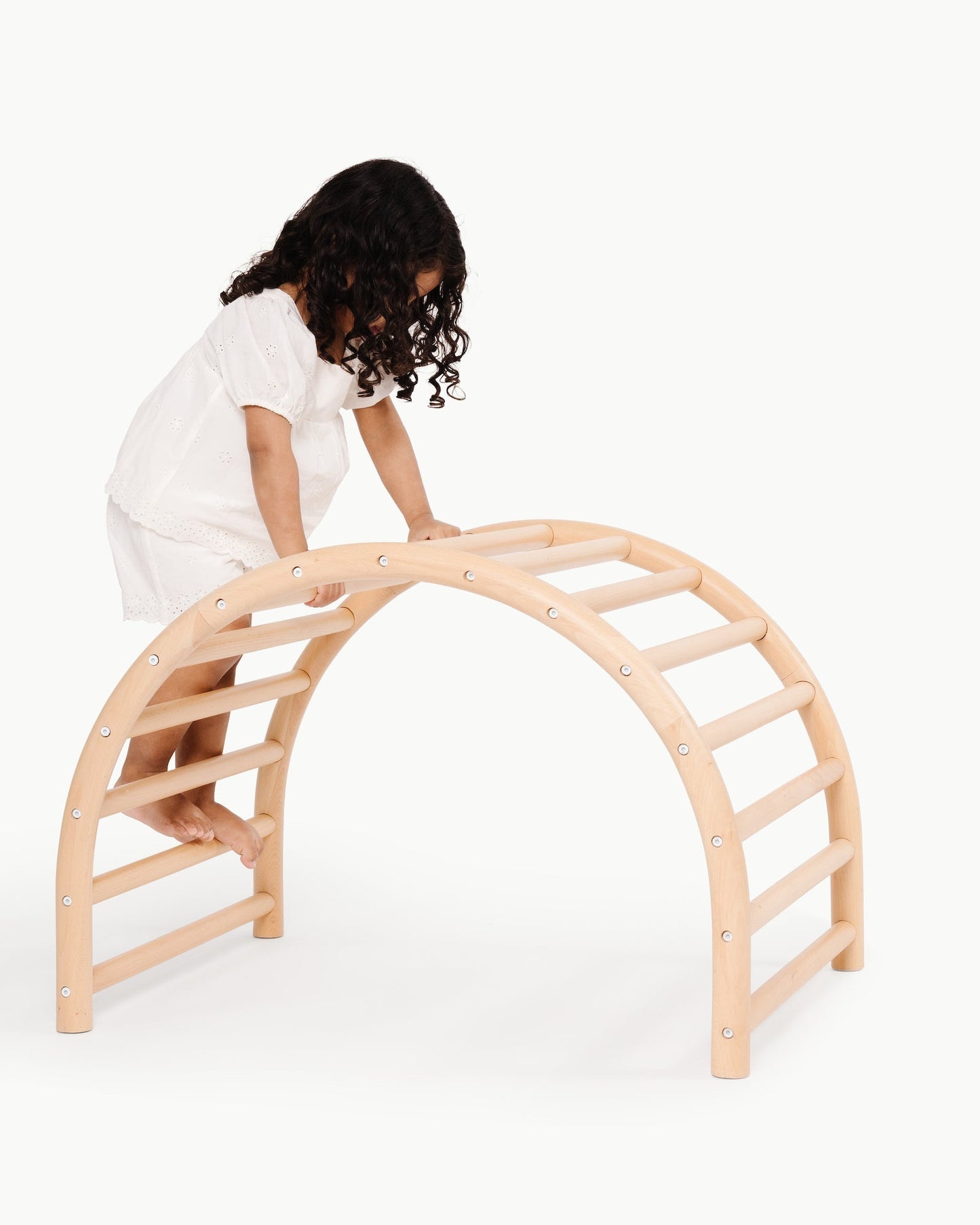 Child climbing on a wooden arch structure against a white background