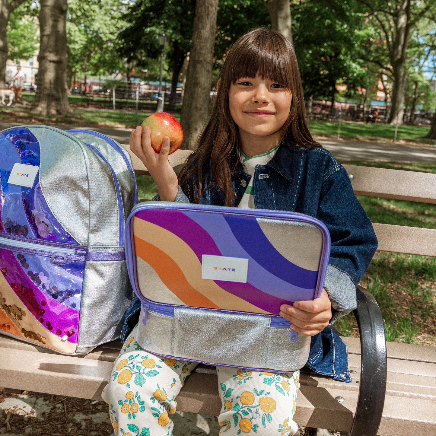 Child holding a colorful lunch bag in a park