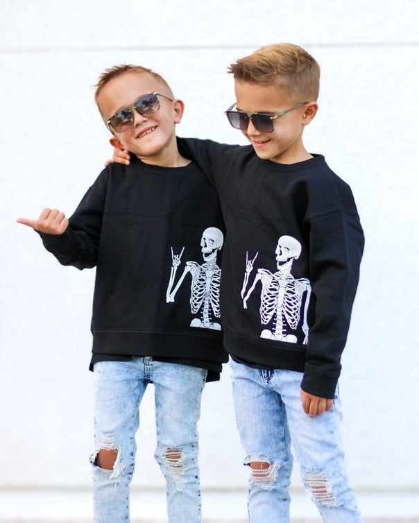 Two children wearing black sweatshirts with skeleton designs and sunglasses, standing against a white background.