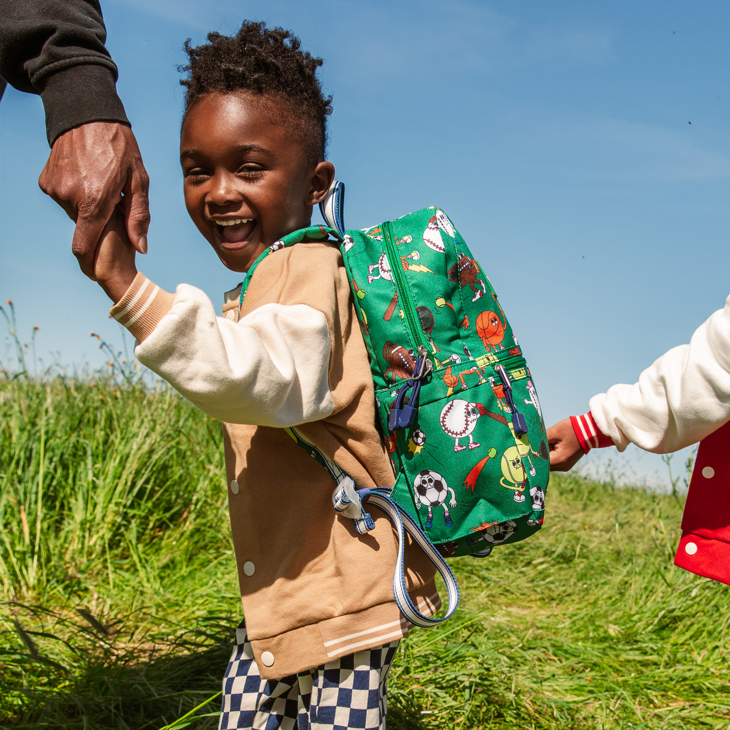 Child with a colorful backpack holding hands outdoors on a sunny day