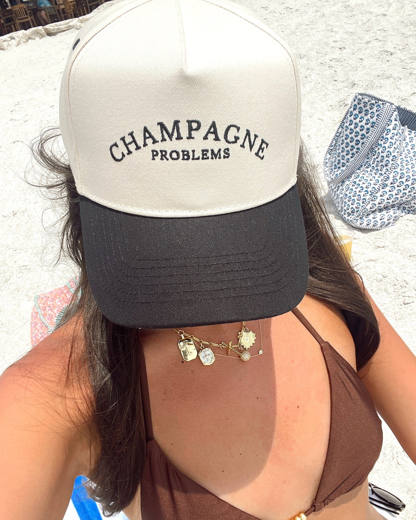 Person wearing a cap with 'Champagne Problems' text, sitting outdoors.