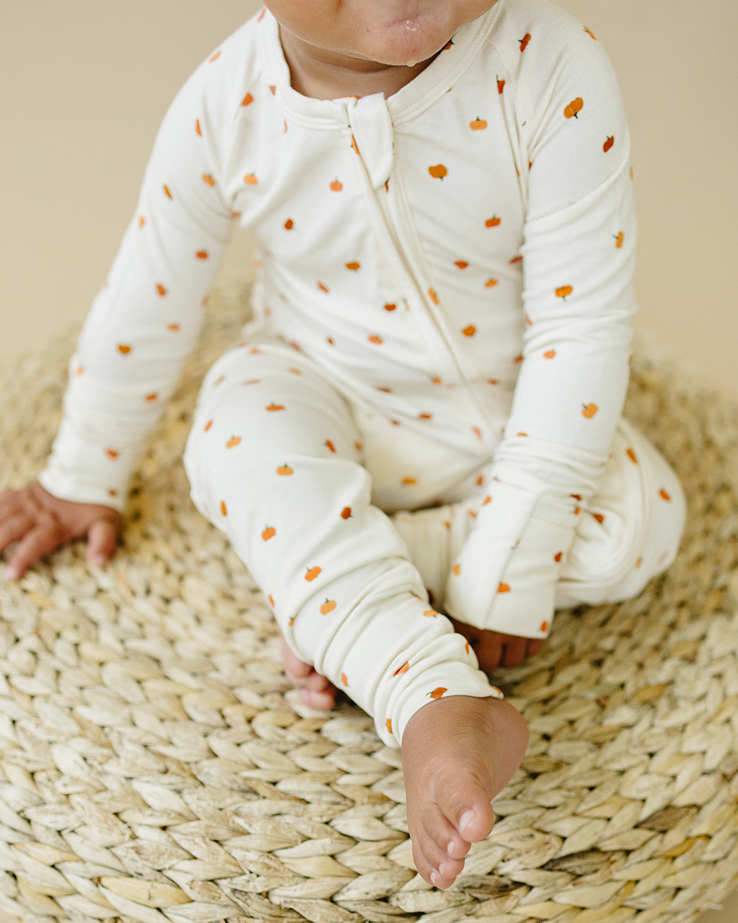 Baby in a white outfit with orange polka dots sitting on a woven mat.