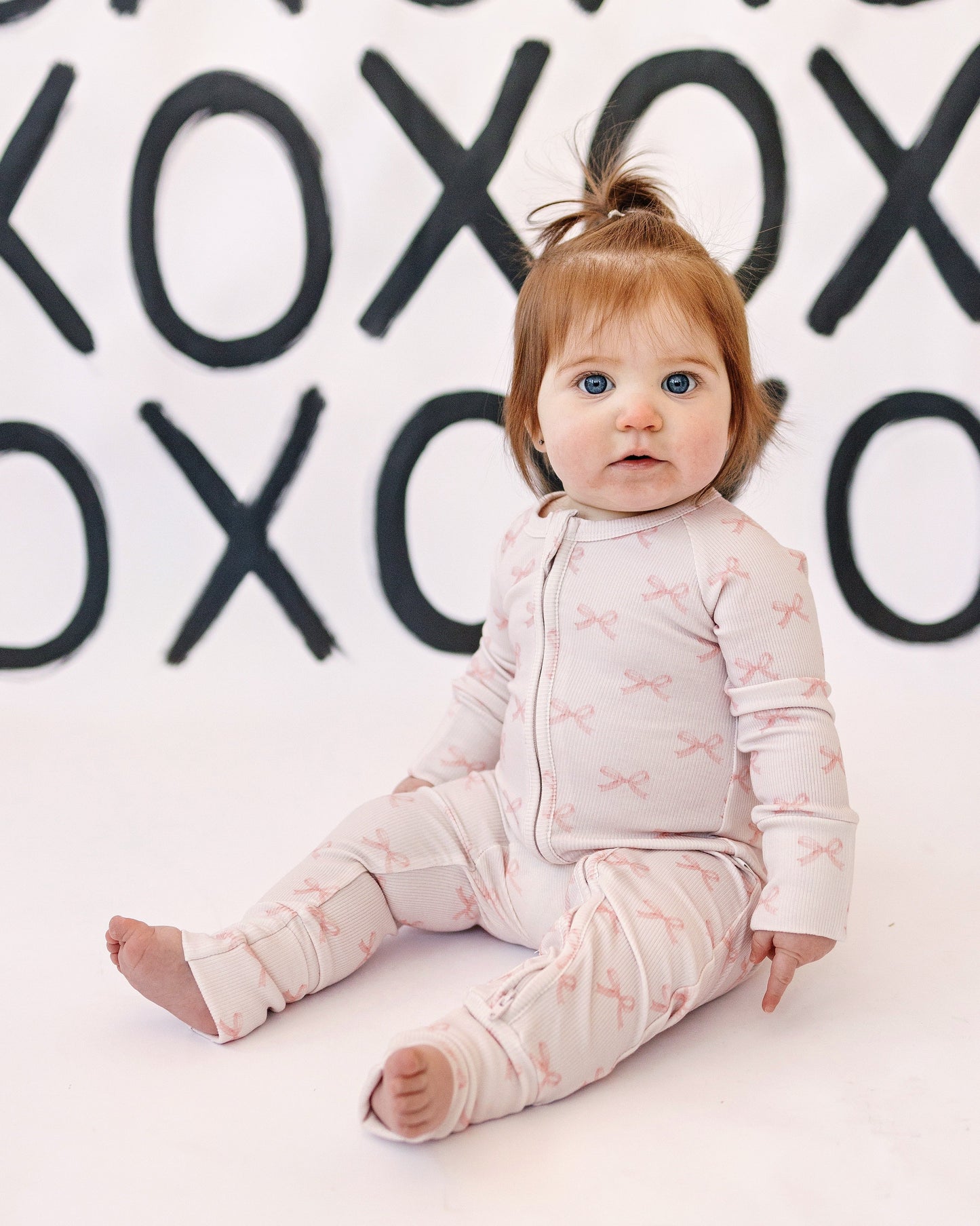 Baby sitting on a white floor with a background of black 'XO' patterns