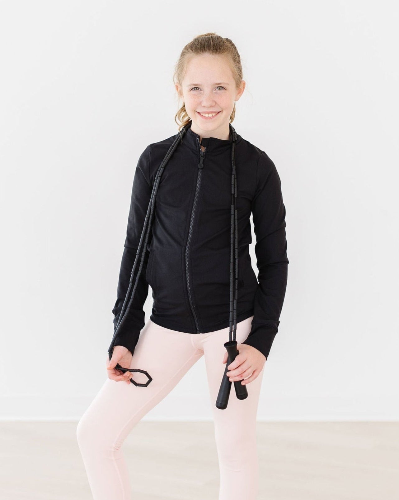 Person wearing a black jacket and pink leggings holding a jump rope on a white background