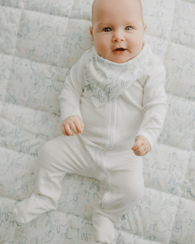 Baby in a white onesie sitting on a textured surface