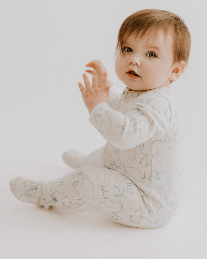 Baby in a bunny onesie pajamas sitting on a white background