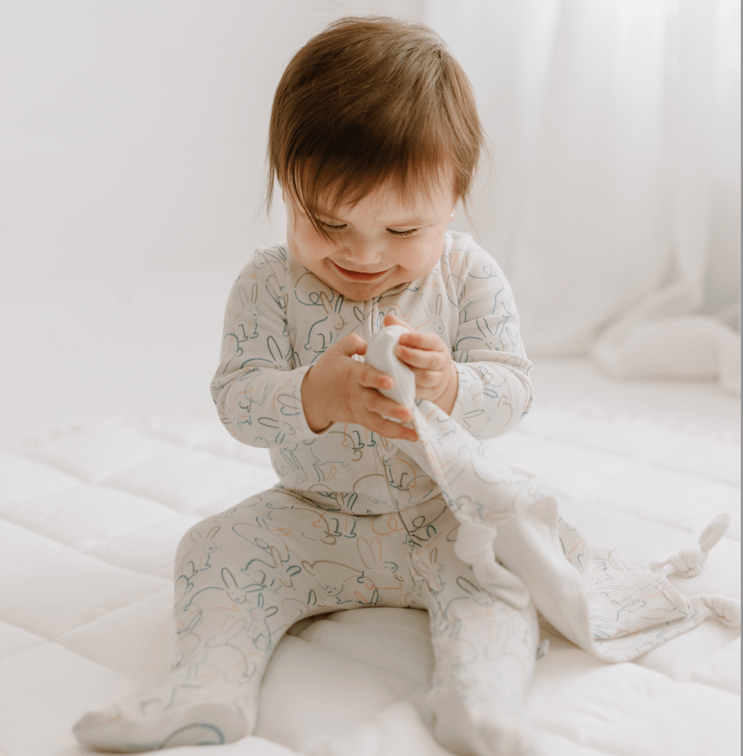 Child in light-colored pajamas sitting on a bed holding a white blanket.