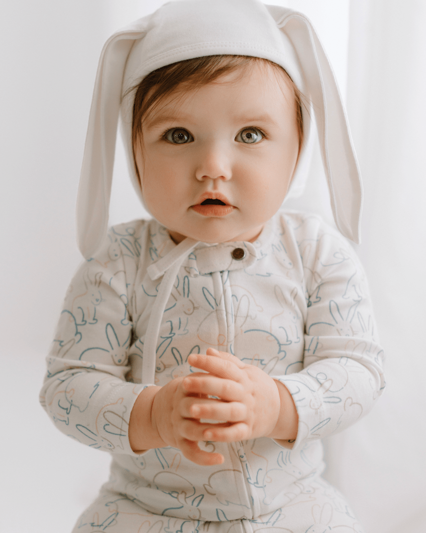Baby wearing a light gray hoodie with bunny ears on a white background