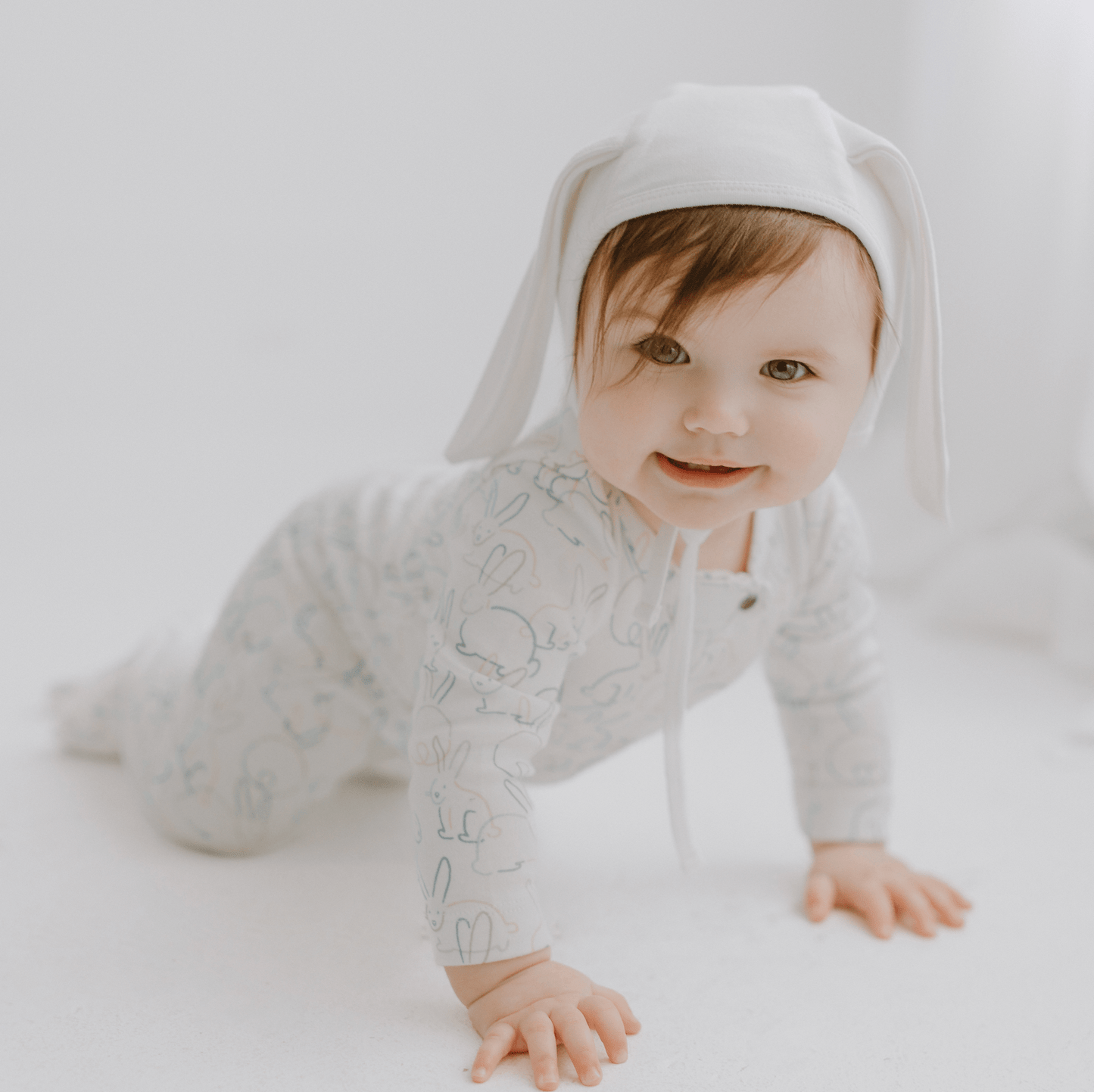 Baby wearing a light gray onesie with bunny ears on a white background
