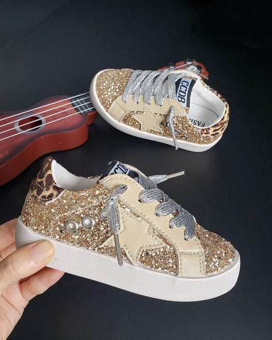 Sparkly sneaker with leopard print and pearl details held by a hand, with a small red guitar in the background.