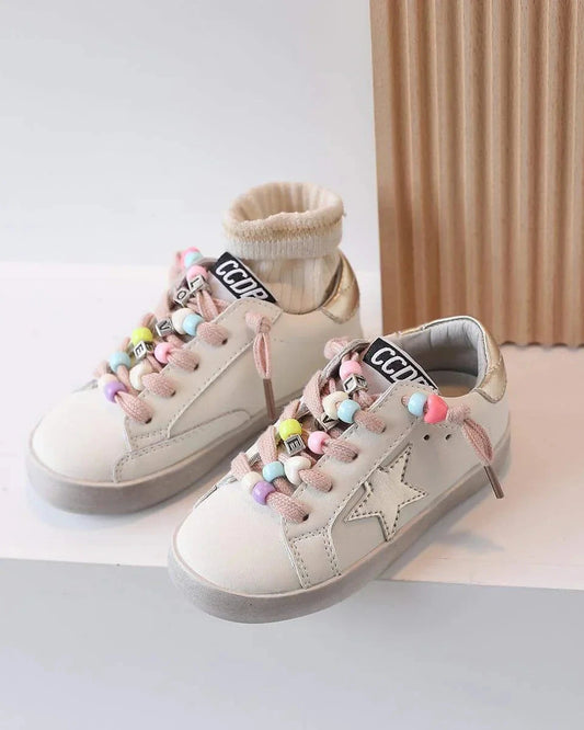 Pair of beige sneakers with colorful pom-poms on a light background
