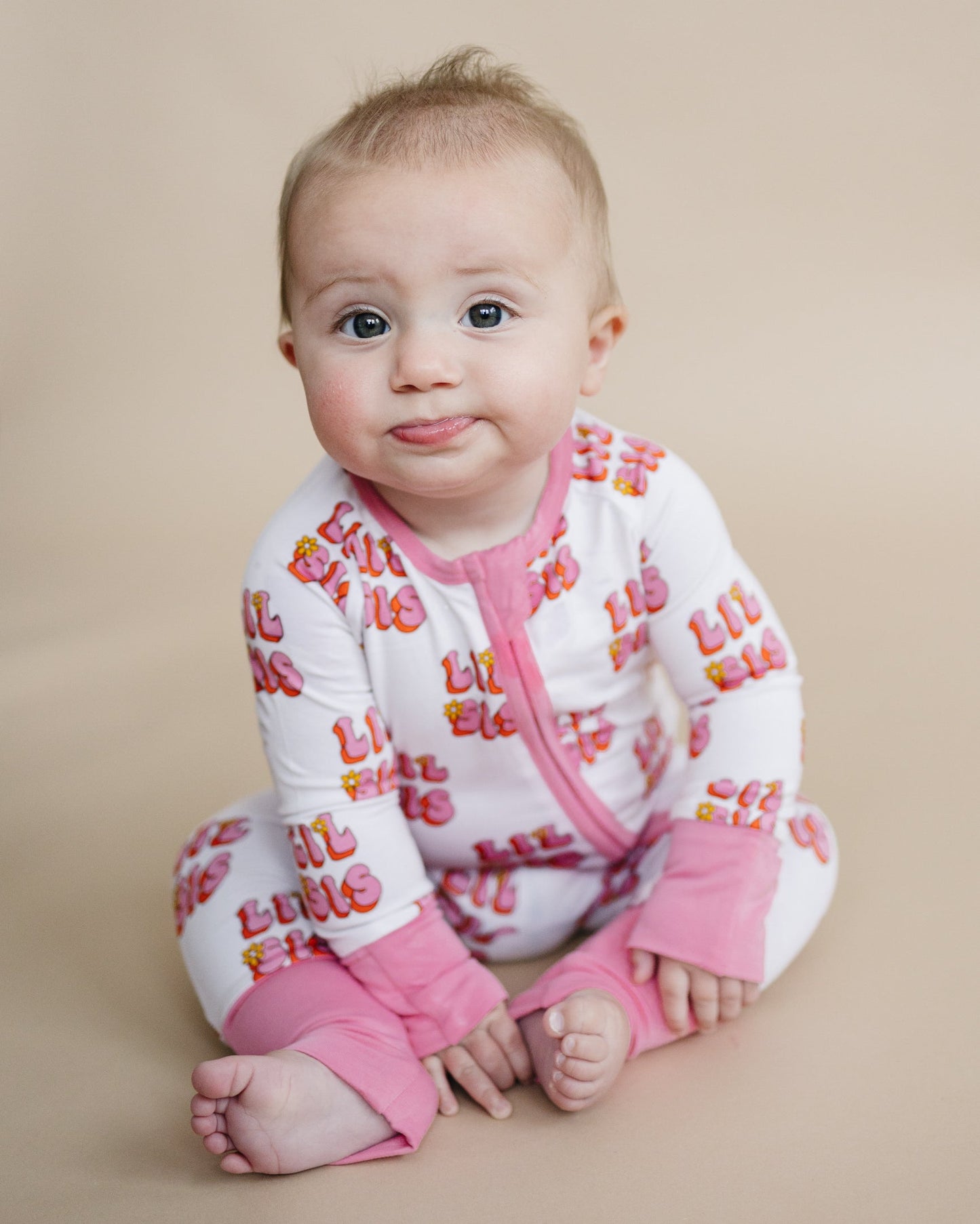 Baby wearing a white outfit with colorful text and pink pants on a beige background