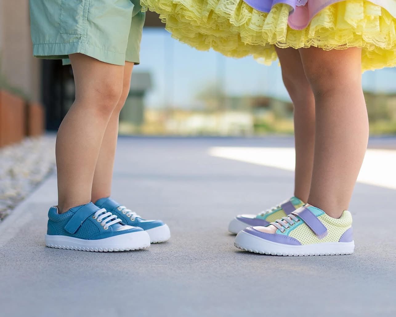 Two pairs of children's shoes, one blue and one multicolored, on a pavement.
