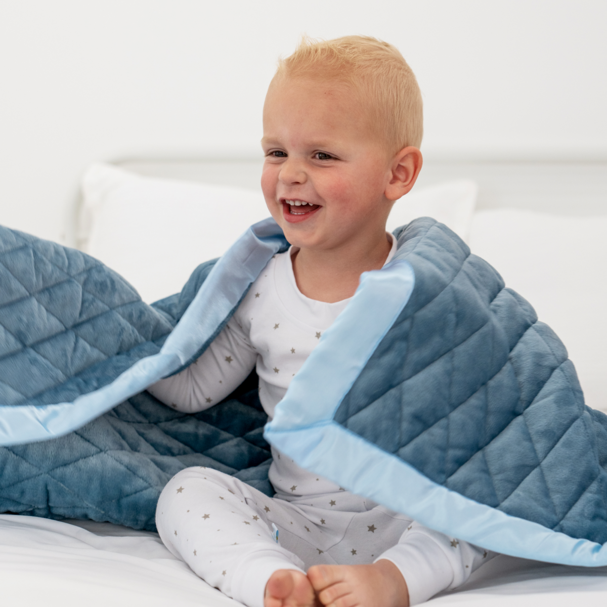 Child wrapped in a blue weighted blanket on a bed