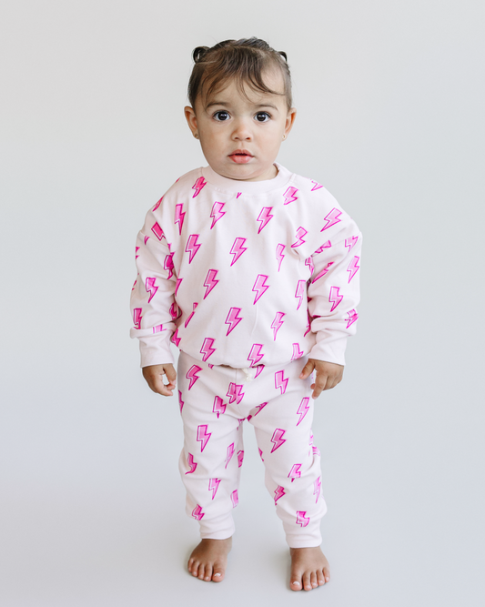 Child wearing a white outfit with pink lightning bolt patterns on a plain background