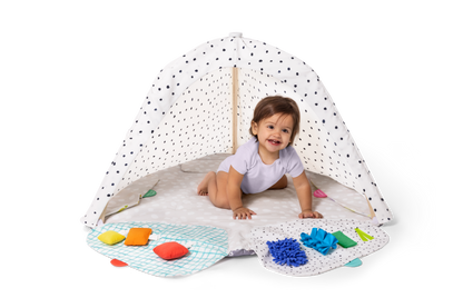 Child playing under a polka dot canopy with toys on a white background