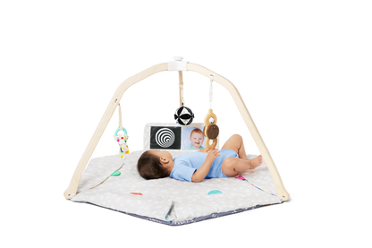 Baby lying on a play mat with a baby gym and toys on a white background