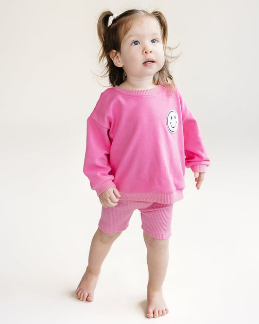 Child wearing a pink outfit with a smiley face on a white background