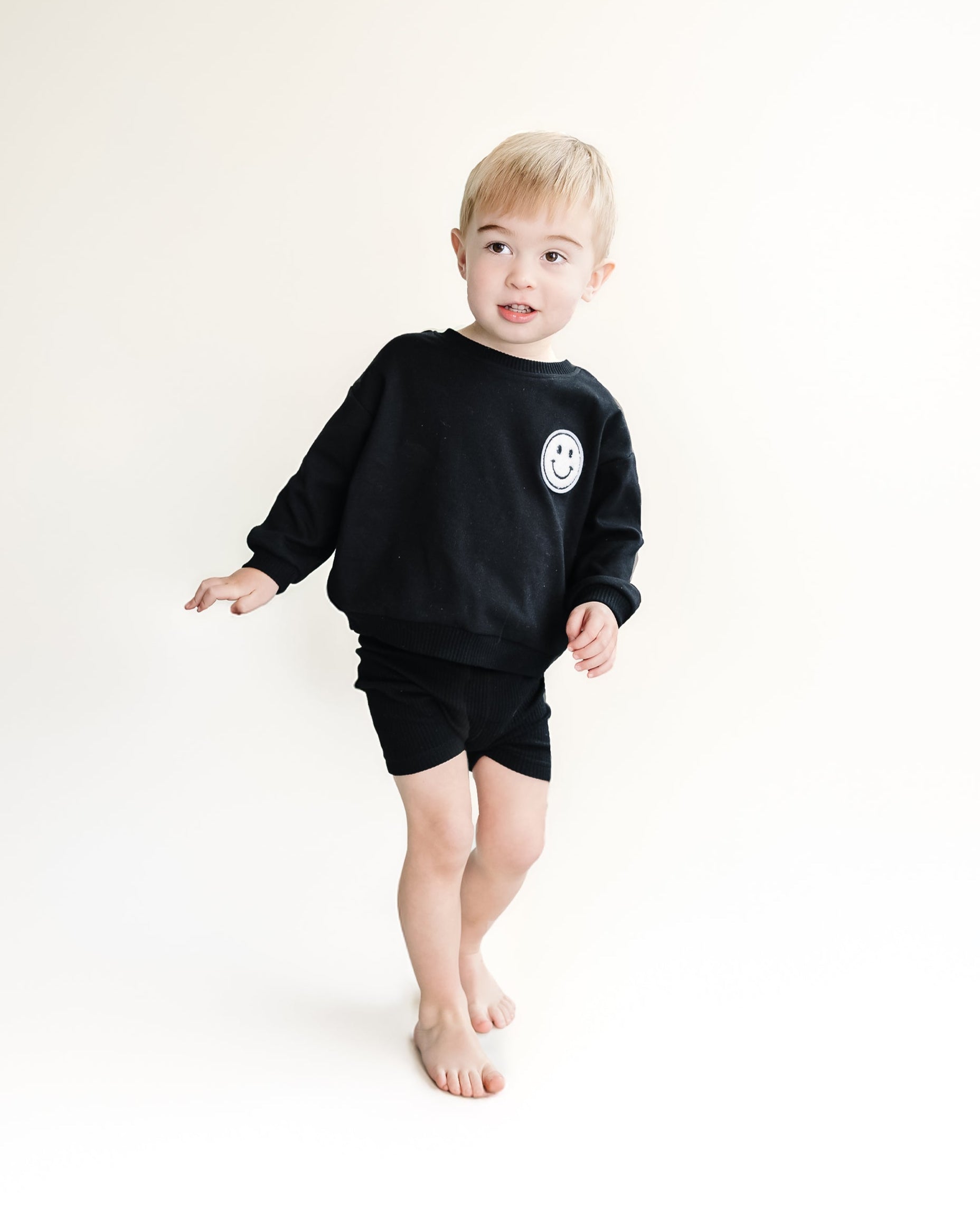 Child wearing a black sweatshirt with a smiley face on a white background