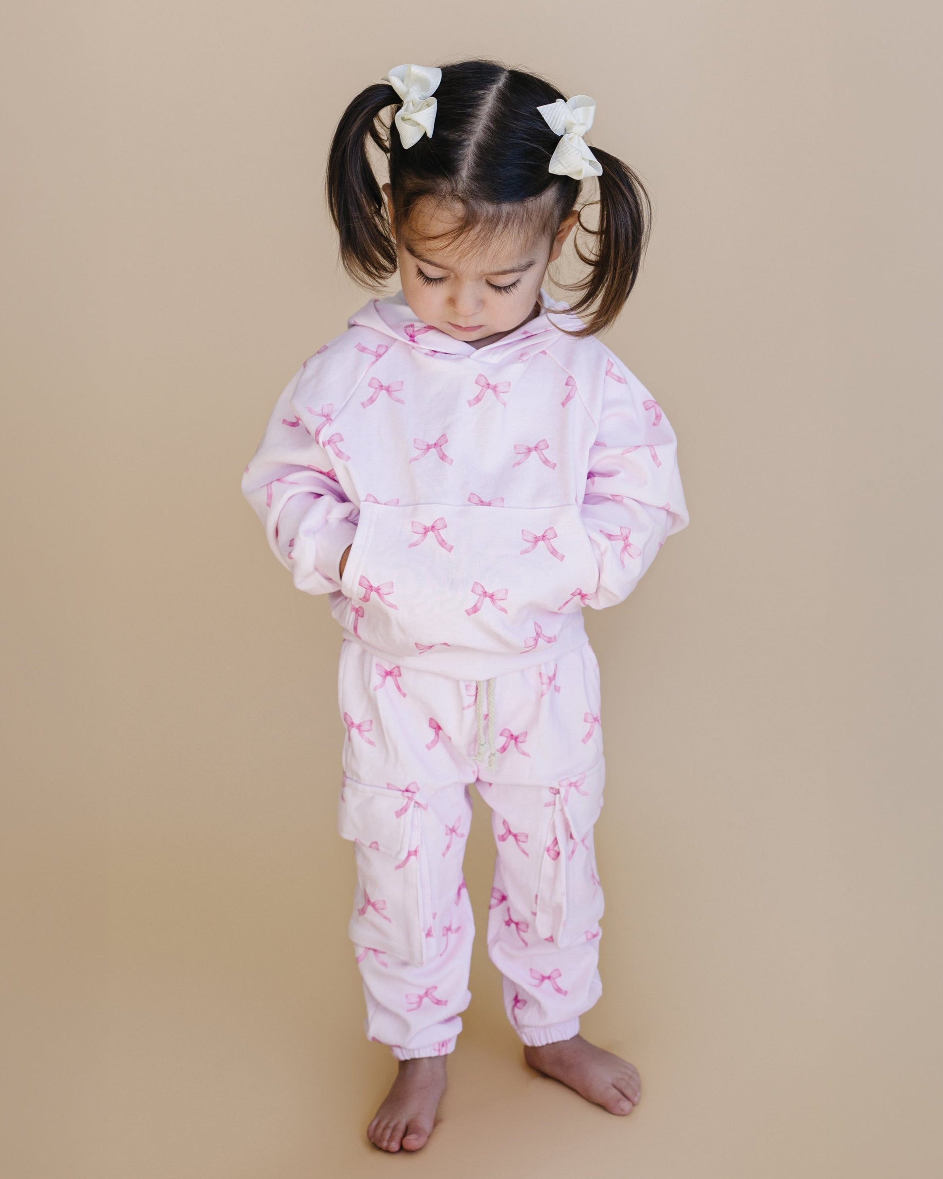 Child wearing a pink pajama set with bow pattern on a beige background