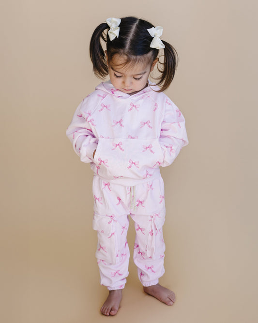 Child wearing a pink pajama set with bow pattern on a beige background