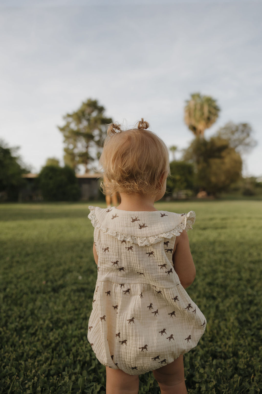 Child in a patterned dress standing in a grassy field with trees in the background