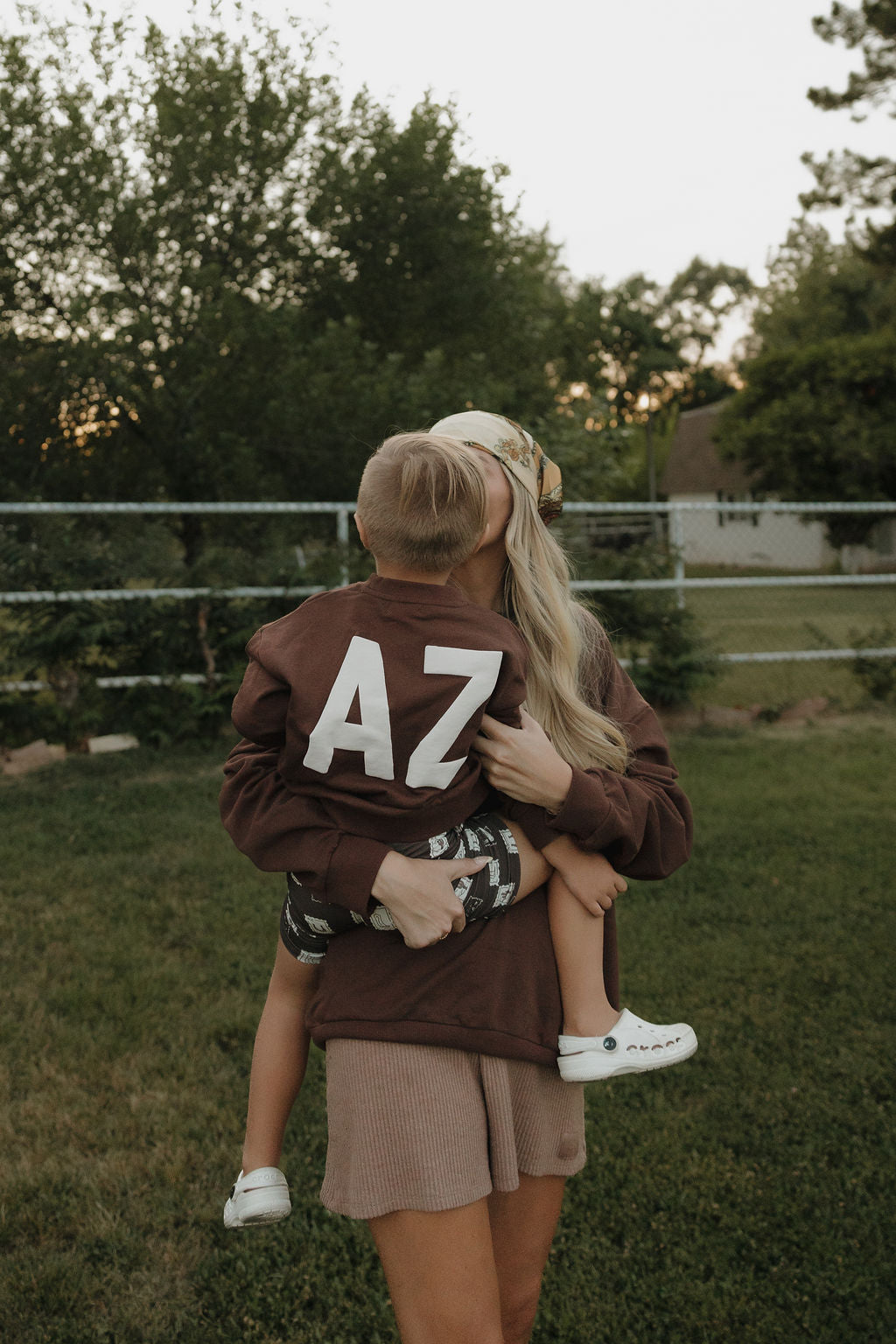 Woman holding a child wearing an 'AZ' jacket in a park setting