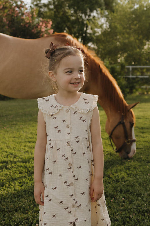 Young girl in a dress standing next to a horse in a grassy field
